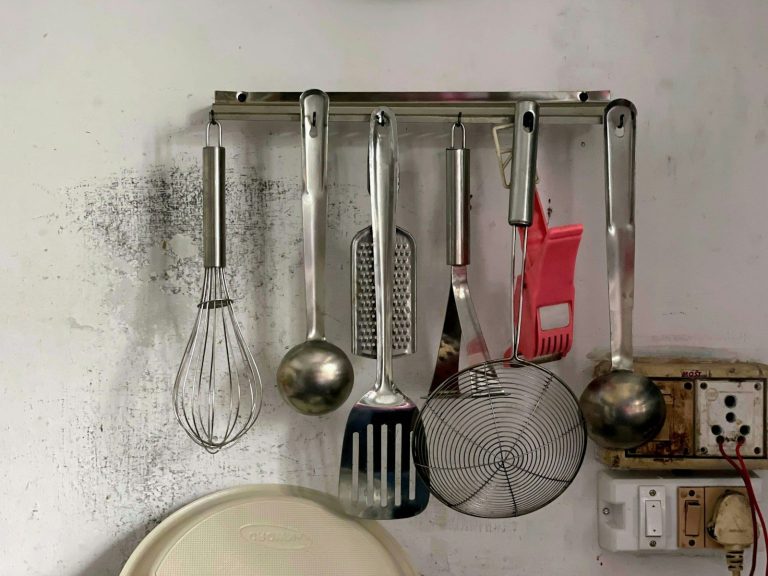 Kitchen utensils hanging from a rail against a wall.