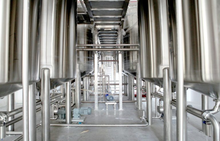 A row of tall stainless steel tanks and pipework inside a food processing hall.