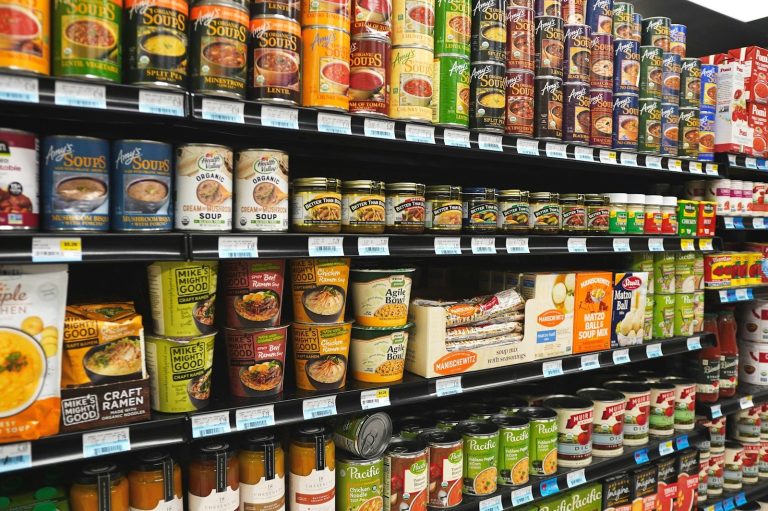 Shelves stocked with rows of canned and packaged foods in a retail store.