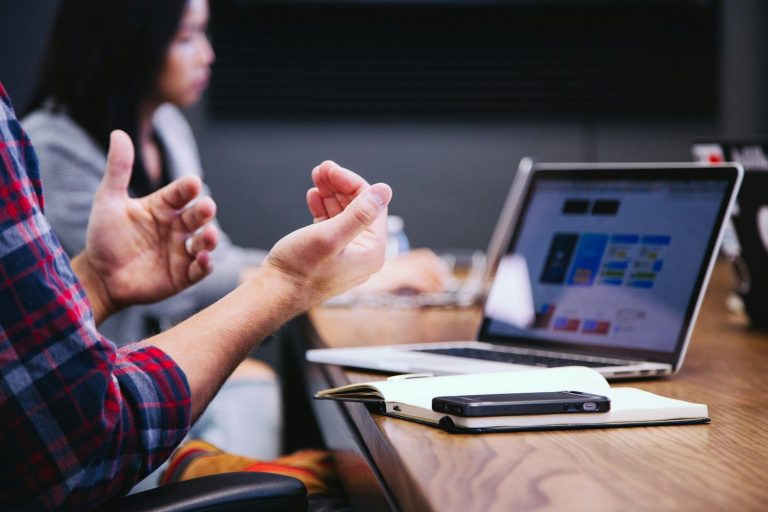Colleagues gesturing while discussing documents around a meeting table.