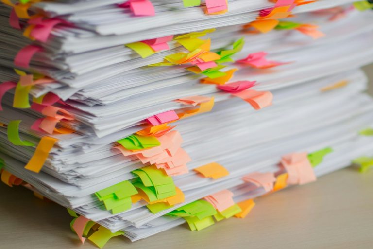 A tall stack of paper documents marked with colourful sticky tabs.