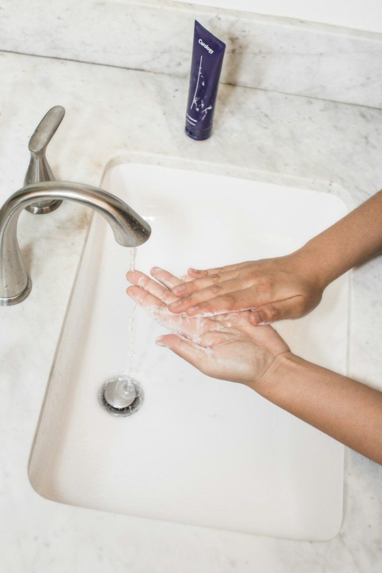 A person washing their hands under a running tap at a clean white basin.
