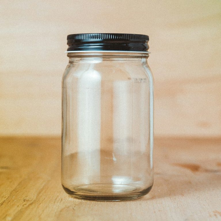 A clear empty glass jar with a metal lid standing on a wooden surface.