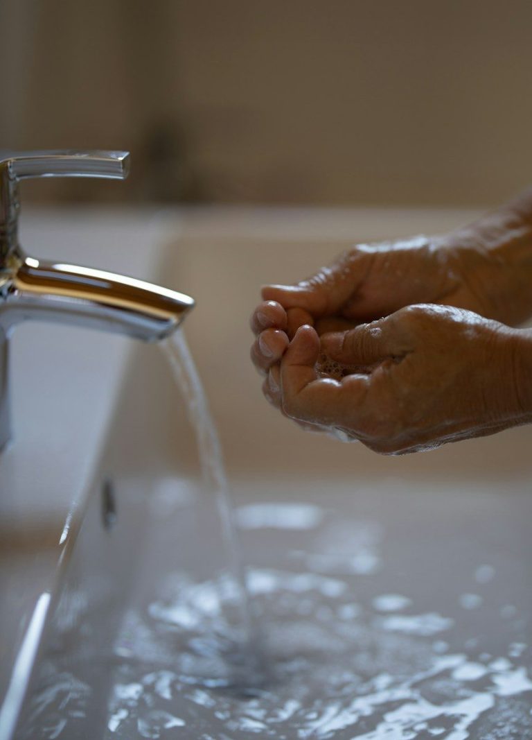 A person rinsing their hands under a running tap at a hand wash sink.