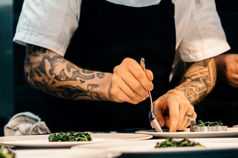 A chef using tweezers to carefully plate a small sample dish.