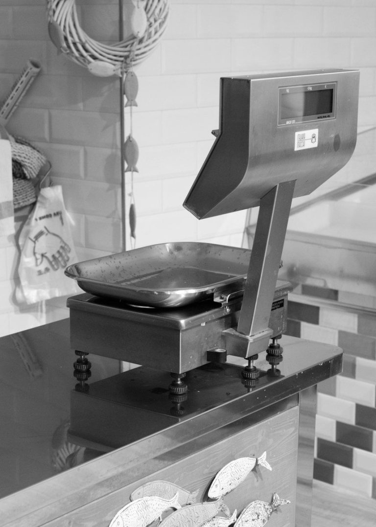 A stainless steel platform scale sits on a bench in a food preparation area.