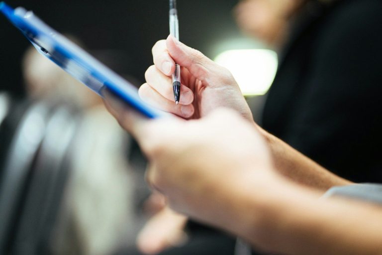 A hand writing notes with a pen on a notepad.