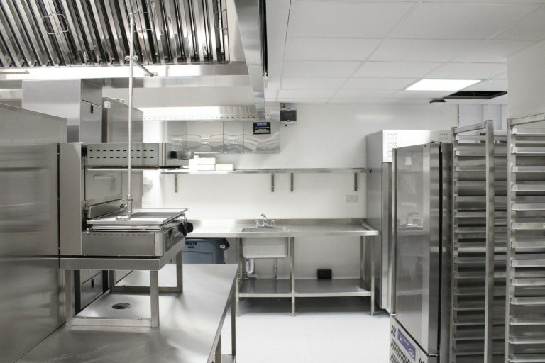Stainless steel commercial kitchen with cooking equipment and trolley racks