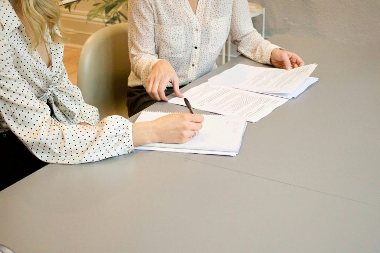 Two people seated at a table reviewing documents and writing notes during a planning meeting.