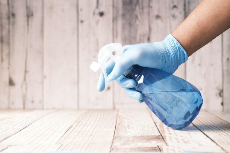A gloved hand holds a spray bottle ready to apply a sanitiser to a clean surface.