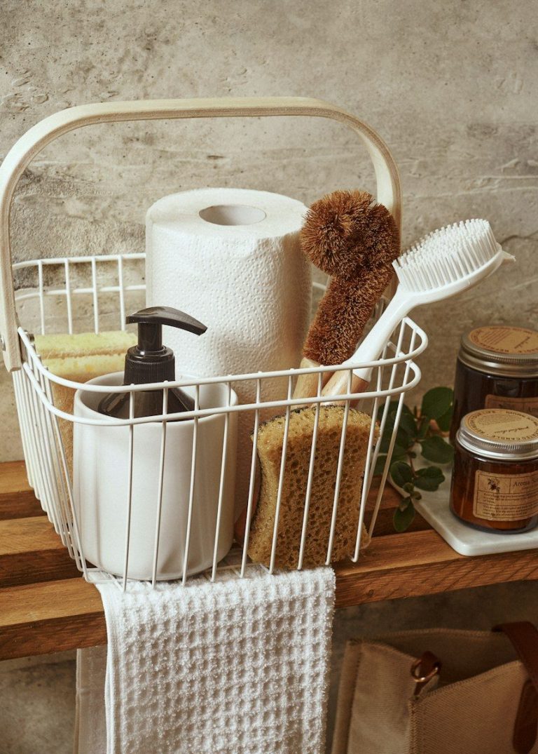 A basket holding brushes, a cloth, a paper towel roll, and a pump bottle of cleaner.