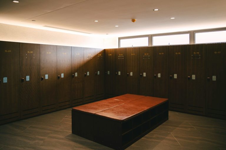 A tidy changing room with dark timber lockers along the walls and a central bench.