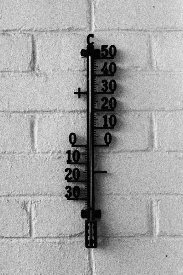 Black outdoor thermometer with a Celsius scale mounted on a white brick wall