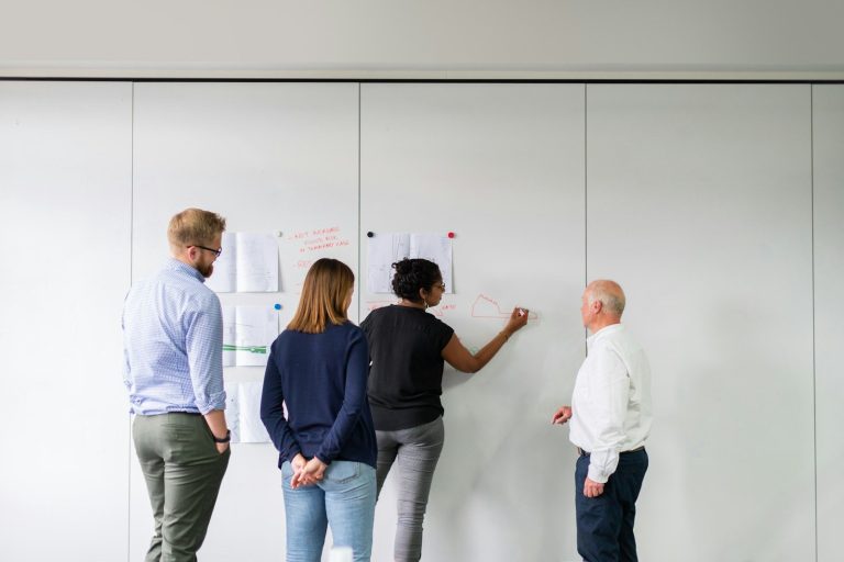 Four colleagues standing at a whiteboard discussing a plan