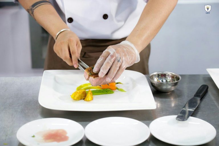 A food handler wearing disposable gloves and a white uniform prepares a dish by hand.