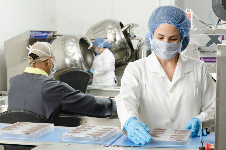 A food worker in a hairnet, mask and gloves handles food in a clean workroom.