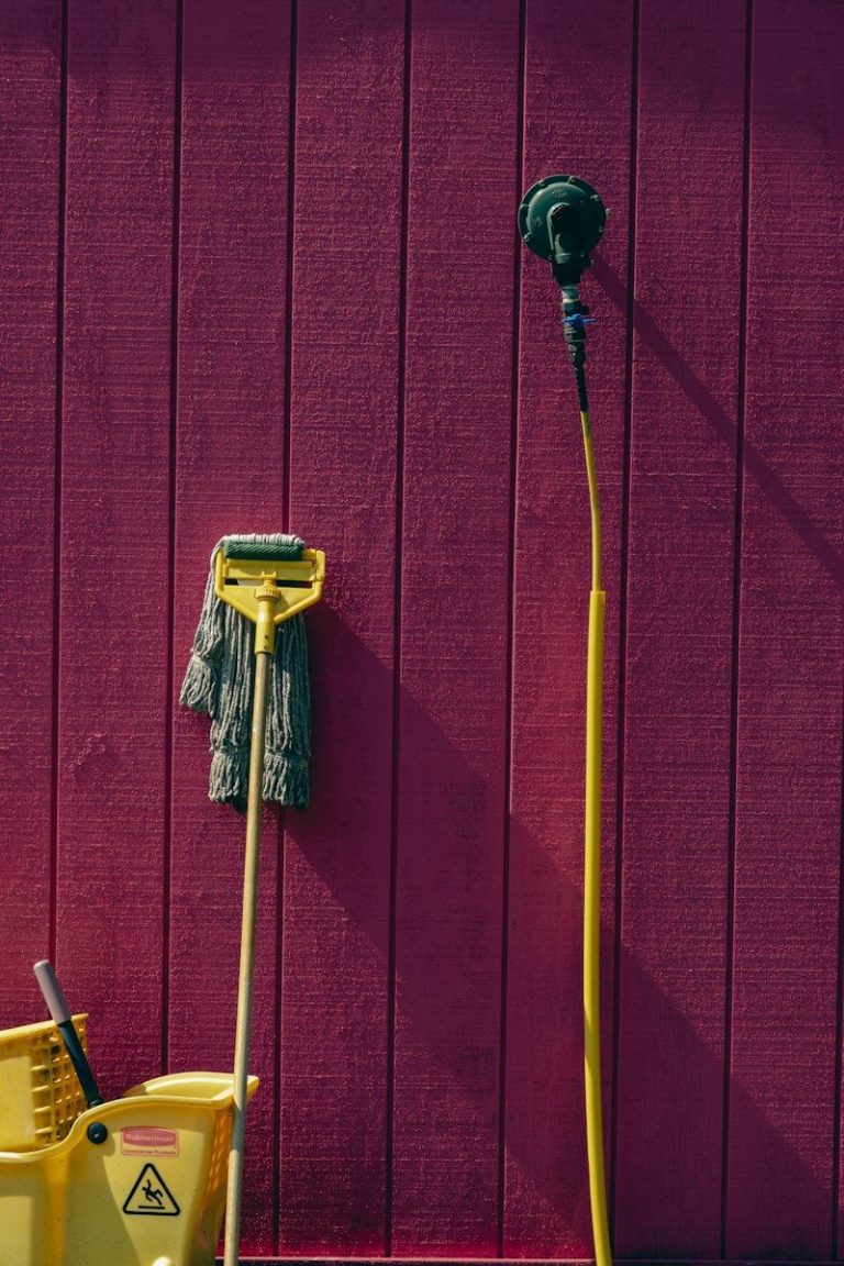 A mop hanging on a wall beside a yellow bucket, ready for use.