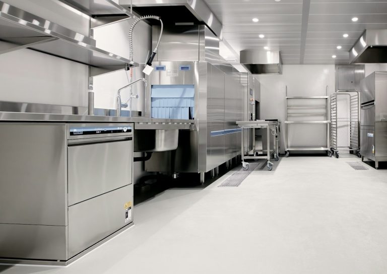 A clean commercial kitchen with stainless steel benches, shelving and a dish washing machine.