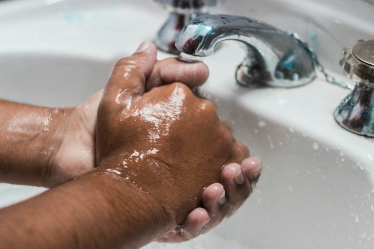 A person lathers soapy hands under a running tap at a washbasin.