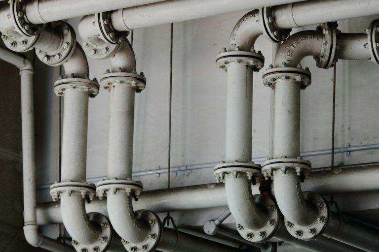 Industrial pipework with flanged joints and valves along a wall.