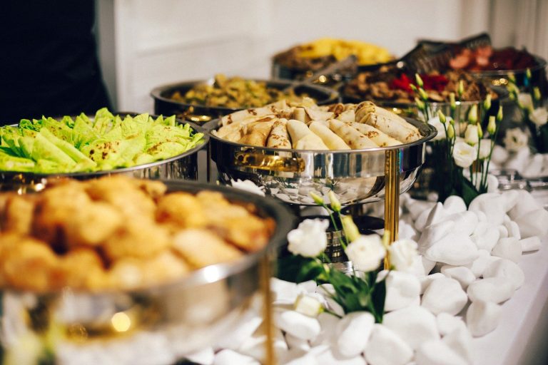 Buffet of prepared dishes in stainless steel serving trays with white flowers