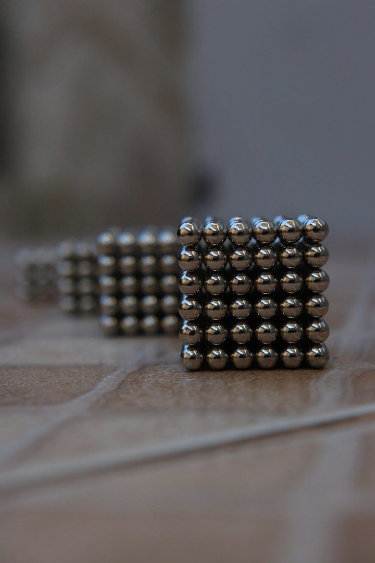 A tight cube made of many small round magnetic steel balls on a grey surface.