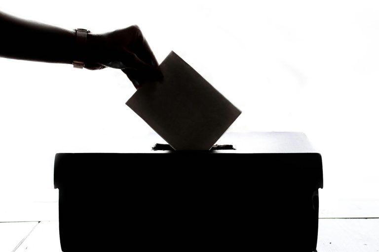 A hand posting a card into a black box, shown in silhouette.
