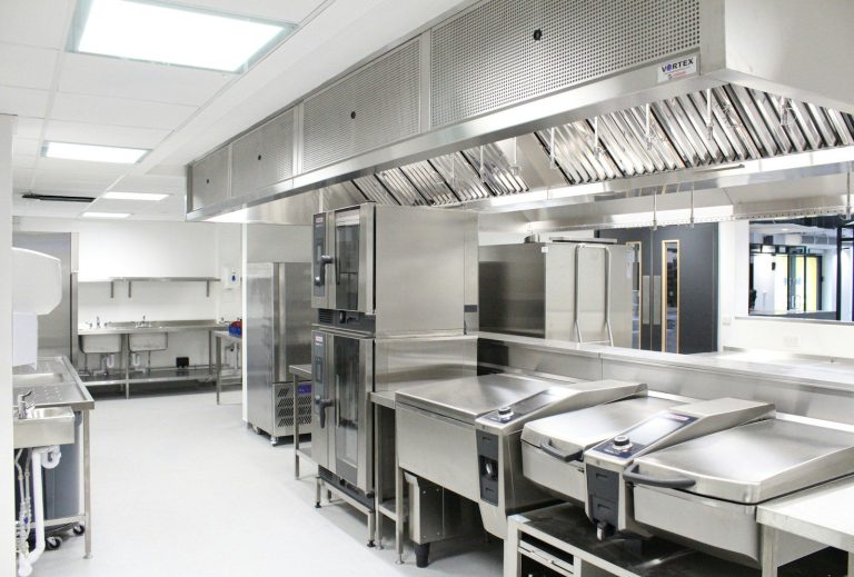 A commercial kitchen with stainless steel equipment, benches, and ventilation.