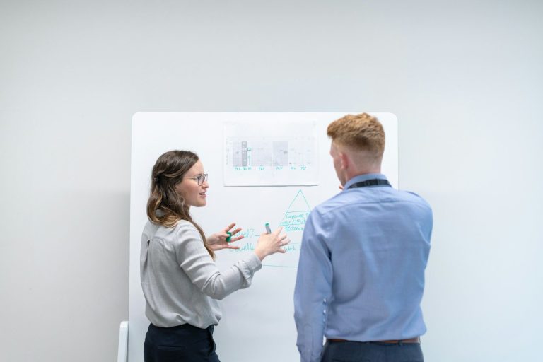 Two colleagues discussing ideas in front of a whiteboard.