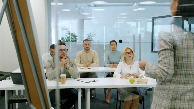 A group of colleagues seated at a table listening to a presenter during a training session.