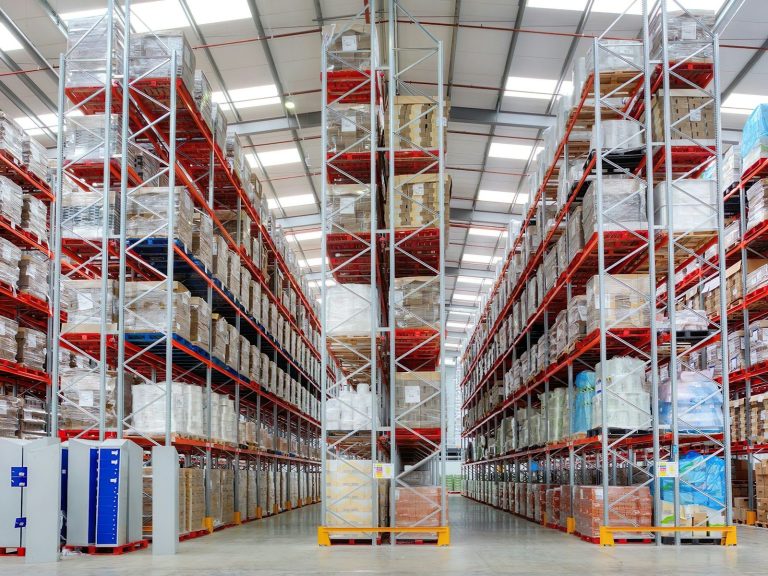 A tidy warehouse aisle with pallet racking and stored goods raised off the floor.