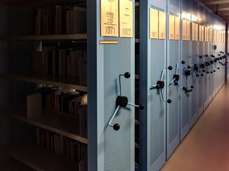 Blue mobile shelving units in a records archive with labelled shelves.