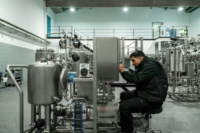 A maintenance technician seated beside stainless steel processing equipment in a clean food processing area.