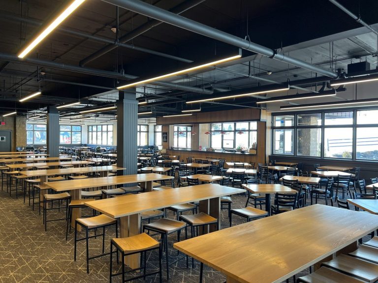 A bright, clean staff dining hall with rows of tables and benches under large windows.
