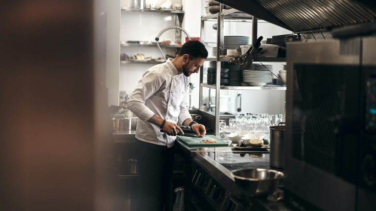 Chef in a white jacket preparing food on a cutting board in a commercial kitchen
